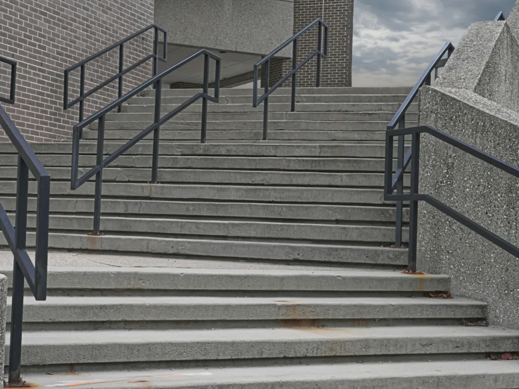 Poured concrete entry stairs with steel handrails leading up to a building entrance