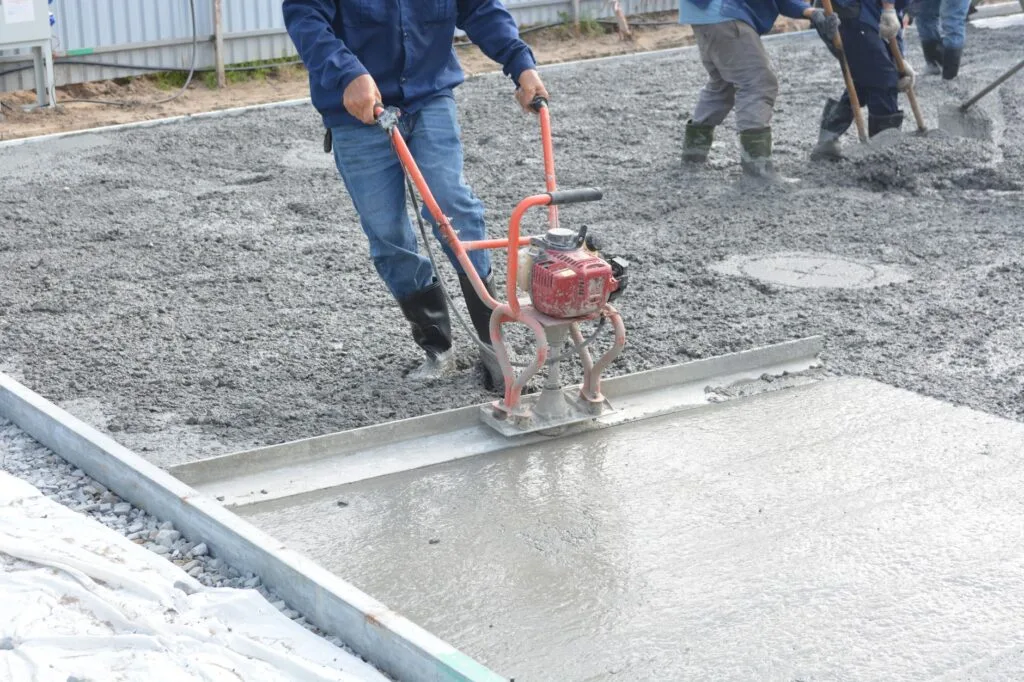 Crew screeding a fresh concrete garage slab pour on a compacted base